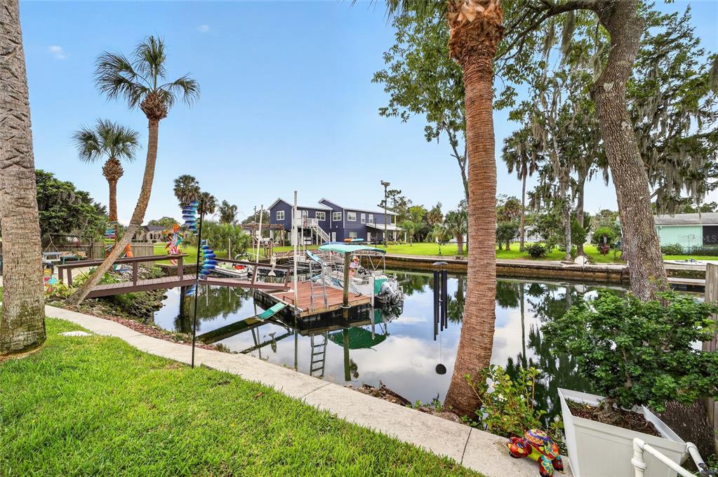 A backyard lawn overlooks a canal with a wooden boat dock and a blue house — 1424 SE 5TH AVENUE, CRYSTAL RIVER, FL
