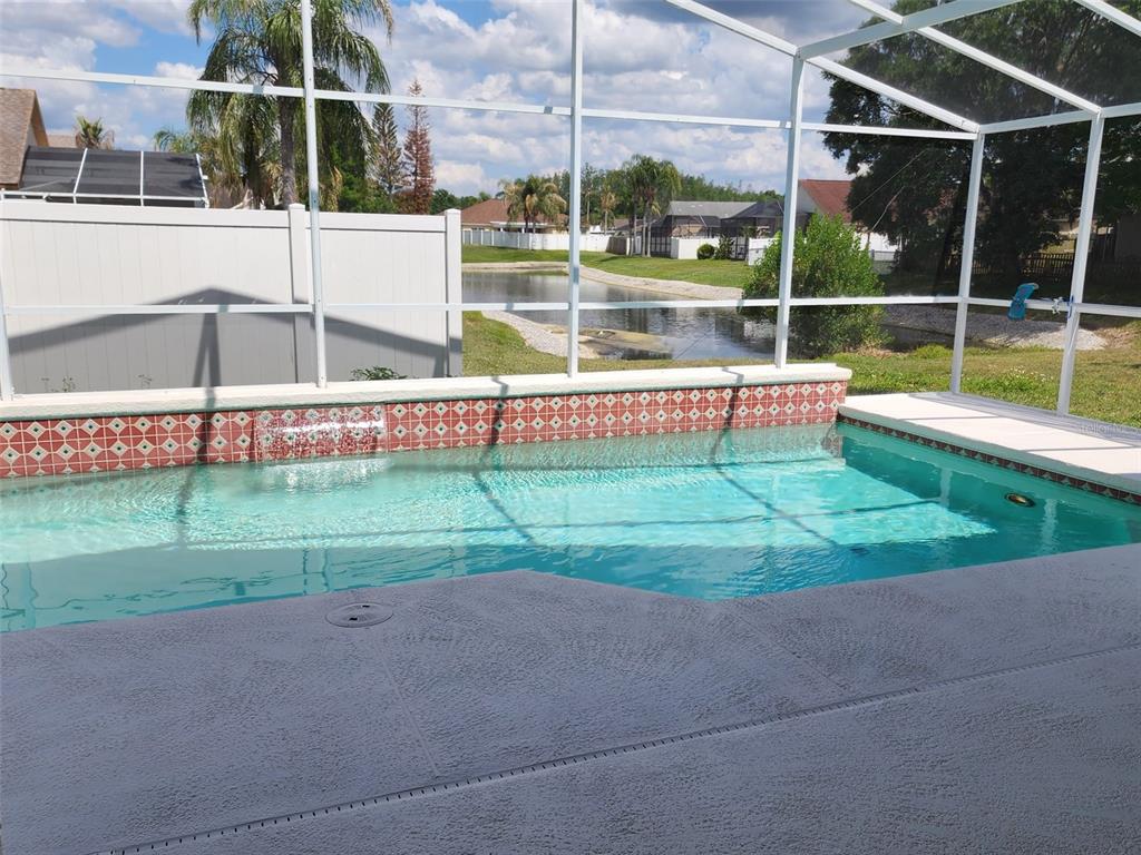 A swimming pool with a decorative tiled wall and water feature inside a screened enclosure — 29545 MORWEN PLACE, WESLEY CHAPEL, FL