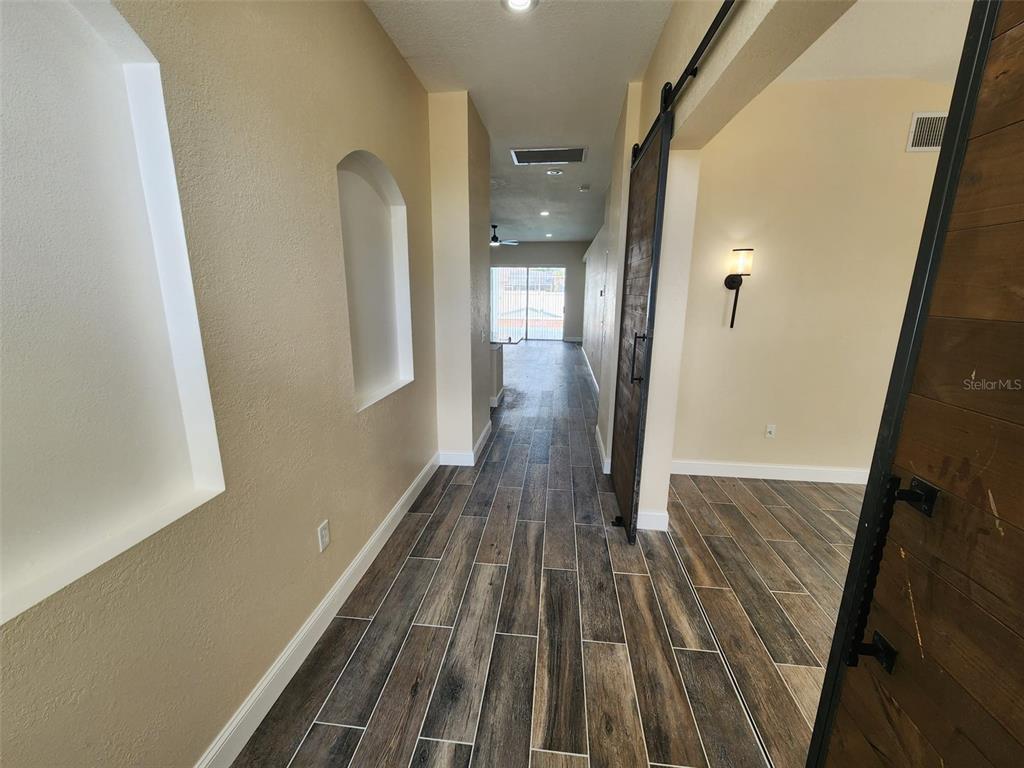 A hallway with wood-look tile flooring leads toward a room with sliding glass doors — 29545 MORWEN PLACE, WESLEY CHAPEL, FL
