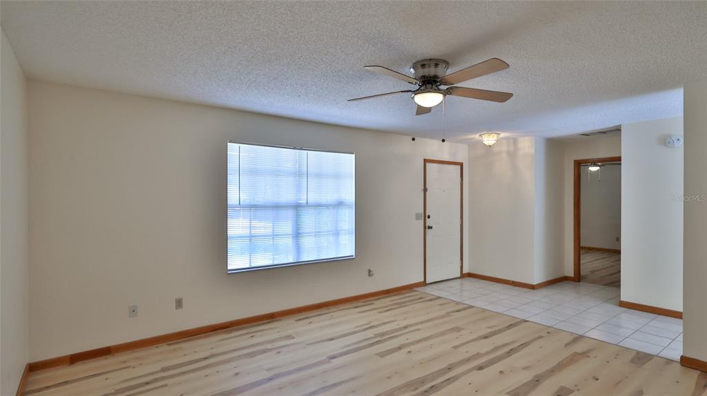 A living room with light wood flooring, a ceiling fan, and a white front door — 3103 JUNIPER DRIVE, EDGEWATER, FL