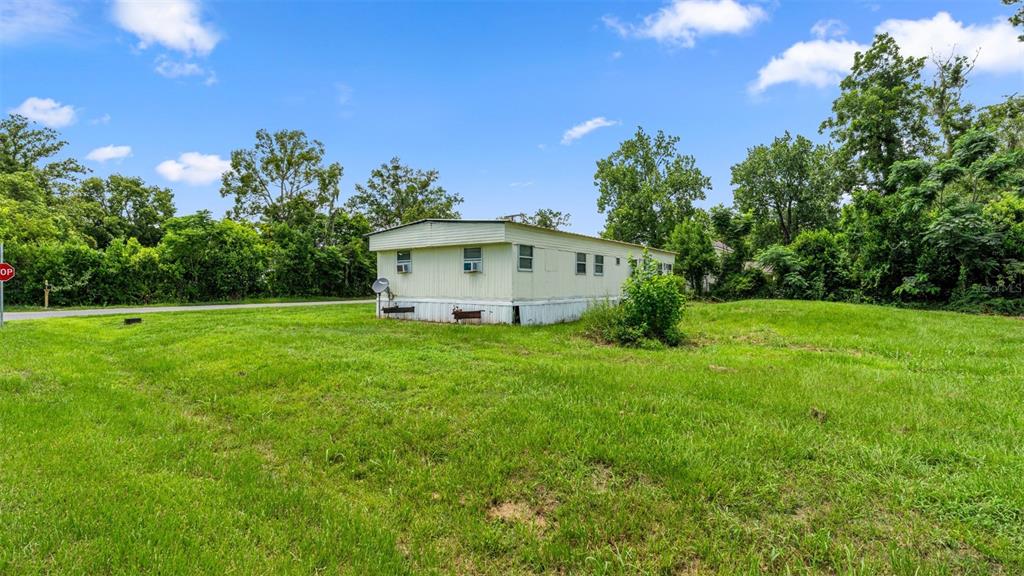 A single-story mobile home sits on a grassy lot surrounded by trees under a blue sky — 5383 ORANGE STREET, HAMPTON, FL