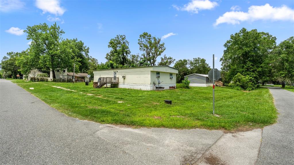 A light-colored mobile home sits on a grassy corner lot between two paved roads — 5383 ORANGE STREET, HAMPTON, FL