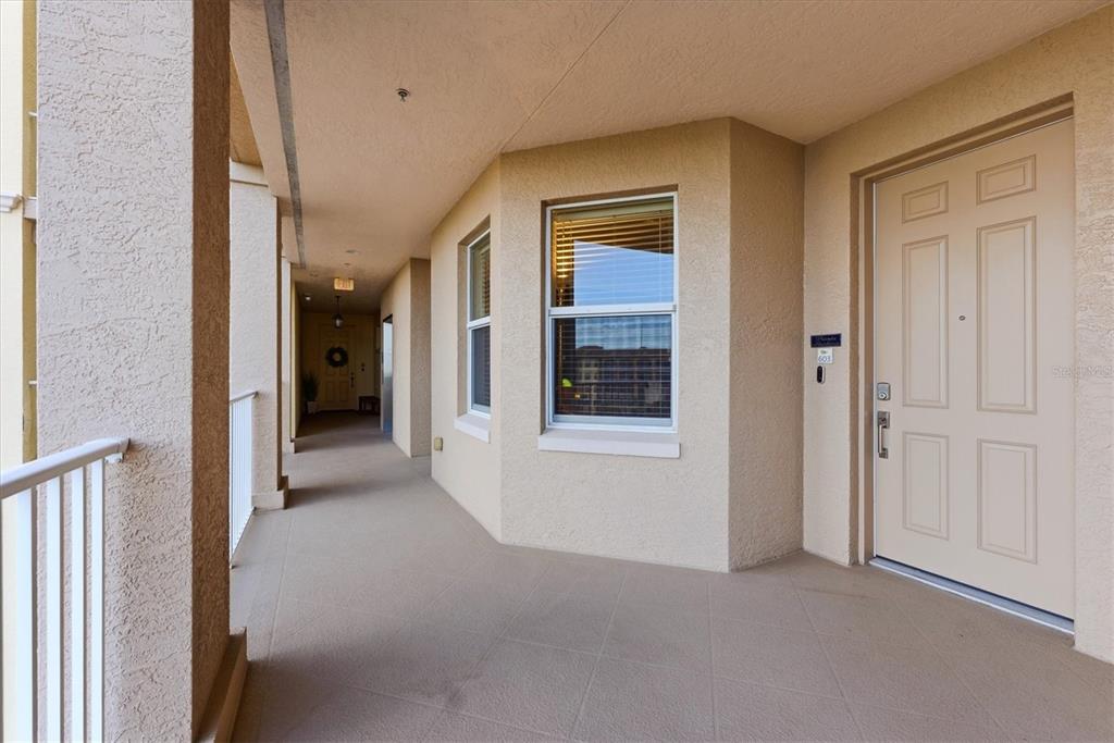 A beige exterior hallway features a window, a light-colored door, and a white railing — 5531 CANNES CIRCLE UNIT 603, SARASOTA, FL