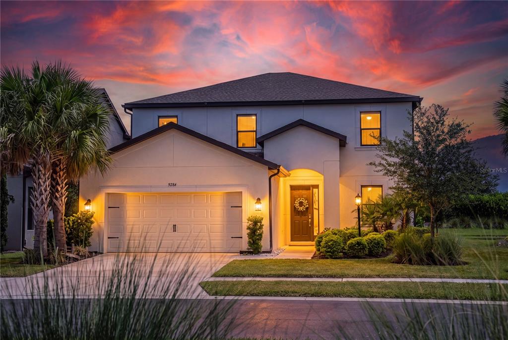 A two-story suburban house with a garage, front entrance, and palm tree at sunset — 9284 TEQUILA SUNRISE DRIVE, SARASOTA, FL