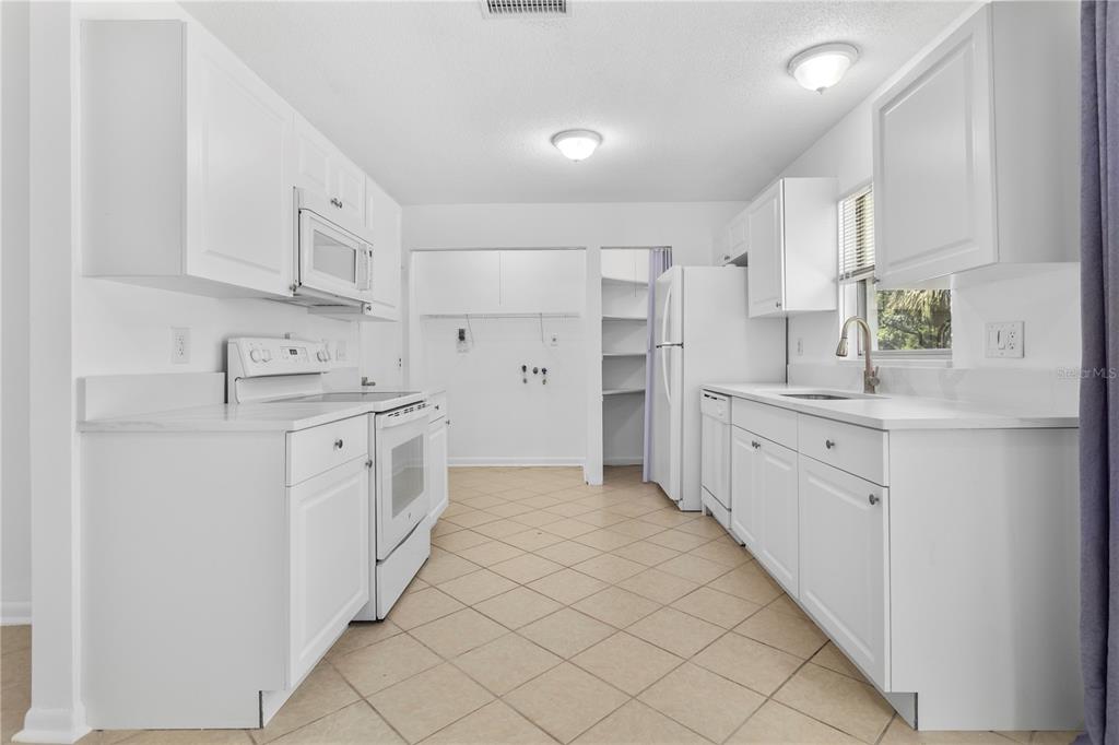A white galley kitchen features tile flooring, white cabinetry, and white appliances — 1923 BONNEVILLE DRIVE, ORLANDO, FL