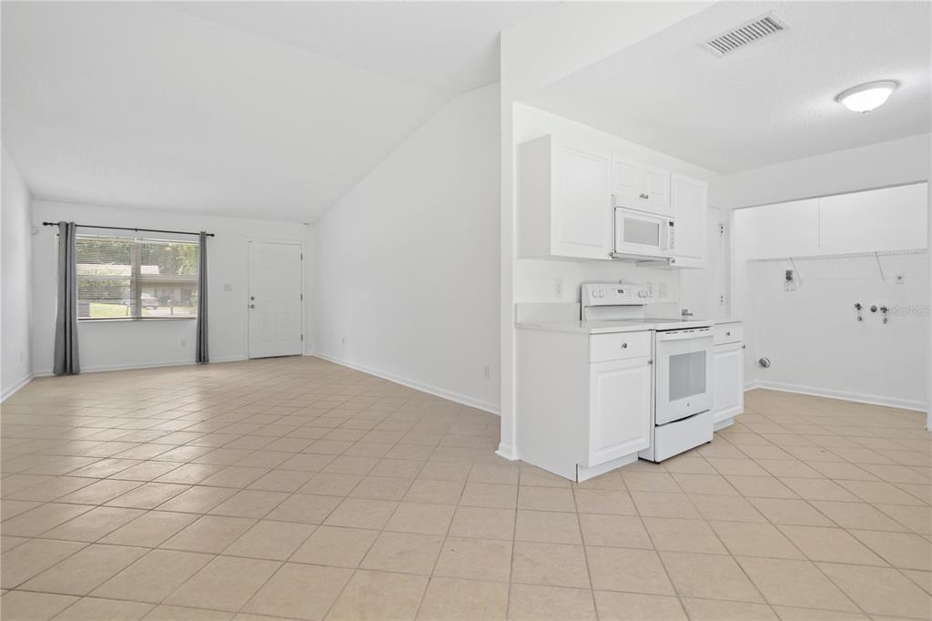 An open-concept room features white kitchen cabinets, white appliances, and light-colored tile flooring — 1923 BONNEVILLE DRIVE, ORLANDO, FL