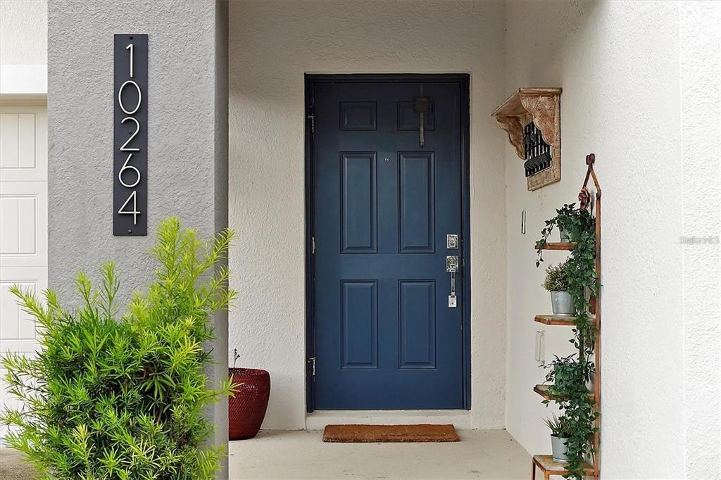 A blue front door is centered on a covered porch with a vertical address sign — 10264 LOVE STORY STREET, WINTER GARDEN, FL