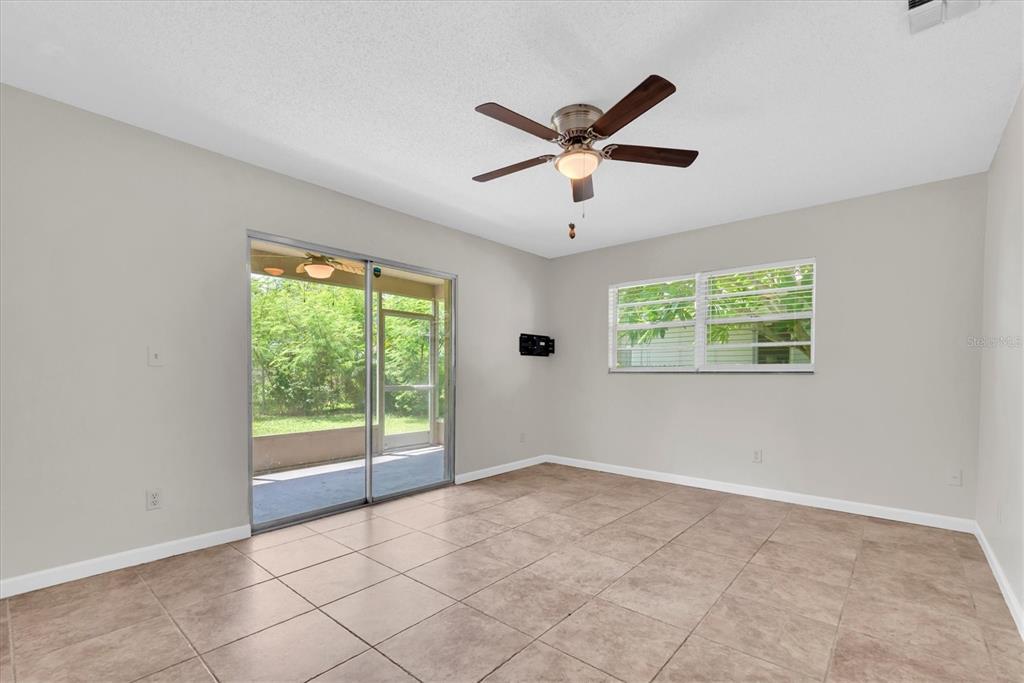 An empty room with beige tile flooring, a ceiling fan, sliding glass doors, and windows — 1521 13TH STREET W, PALMETTO, FL