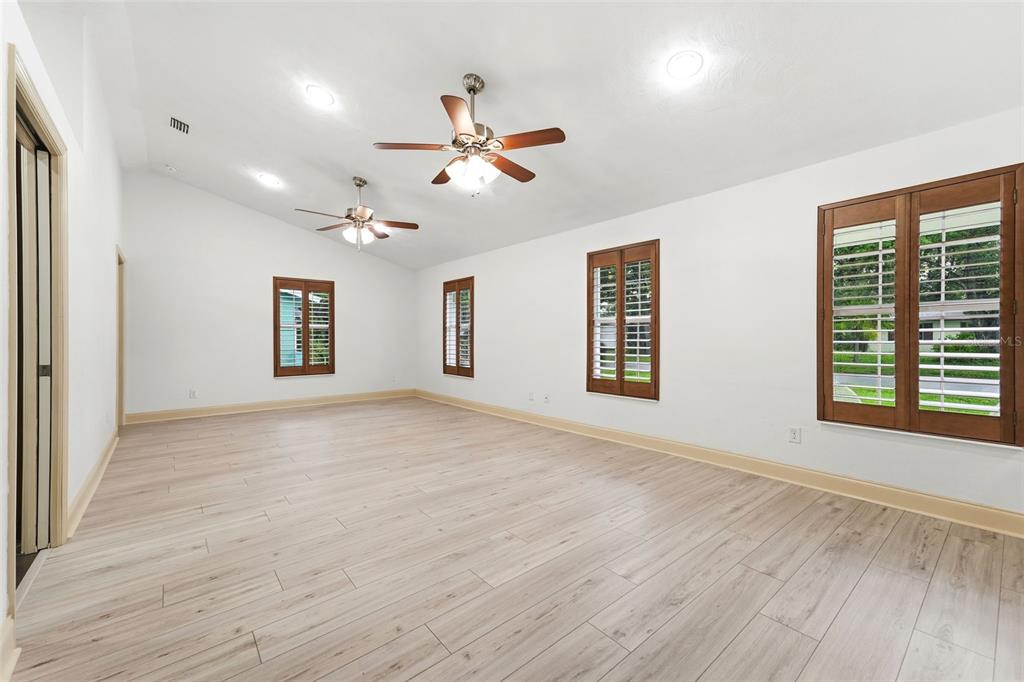 An empty room with light wood-look flooring, white walls, two ceiling fans, and shuttered windows — 59 CRESTWOOD CIRCLE, ORMOND BEACH, FL