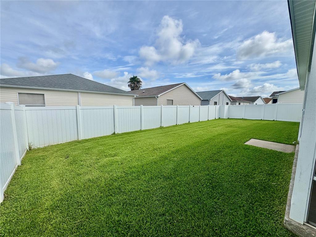 A fenced backyard features a green lawn and a screened-in patio area — 892 NASH LOOP, THE VILLAGES, FL