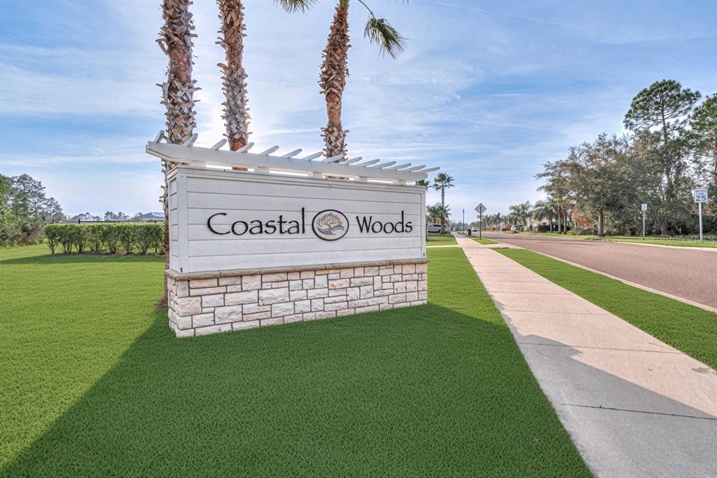 A white sign with the text Coastal Woods stands on a stone base outdoors — 2952 GIBRALTAR BOULEVARD, NEW SMYRNA BEACH, FL
