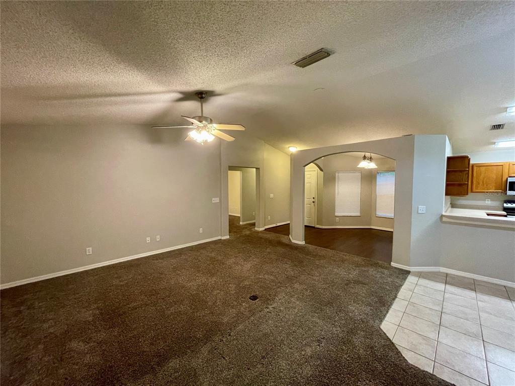 A living room with carpeted flooring, a ceiling fan, and an arched entryway to dining — 12119 WARWICK CIRCLE, PARRISH, FL