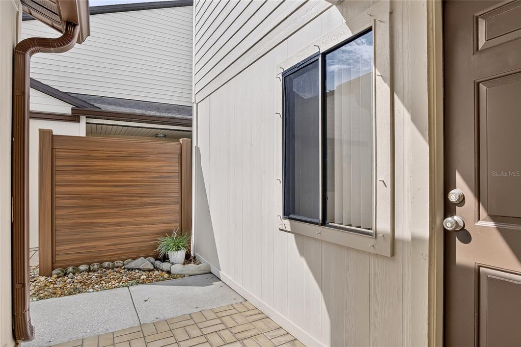 A brown door sits next to a window on a paved patio with a fence — 367 CASTLEWOOD LANE, NEW SMYRNA BEACH, FL