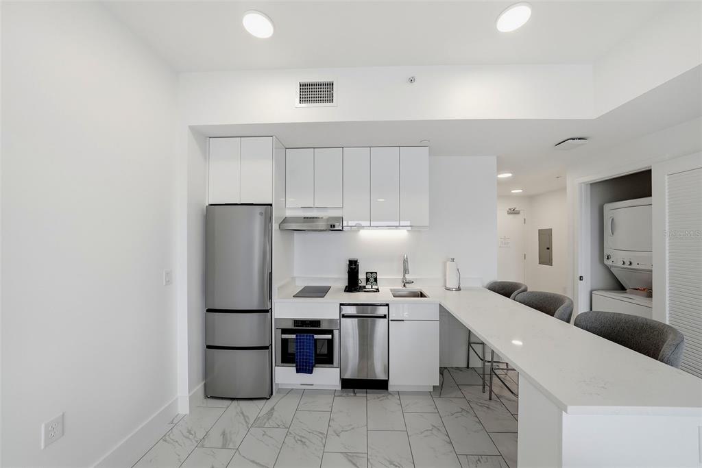 A modern kitchen features white cabinetry, stainless steel appliances, and a white quartz breakfast bar — 411 E SHORE DRIVE UNIT 411, CLEARWATER BEACH, FL