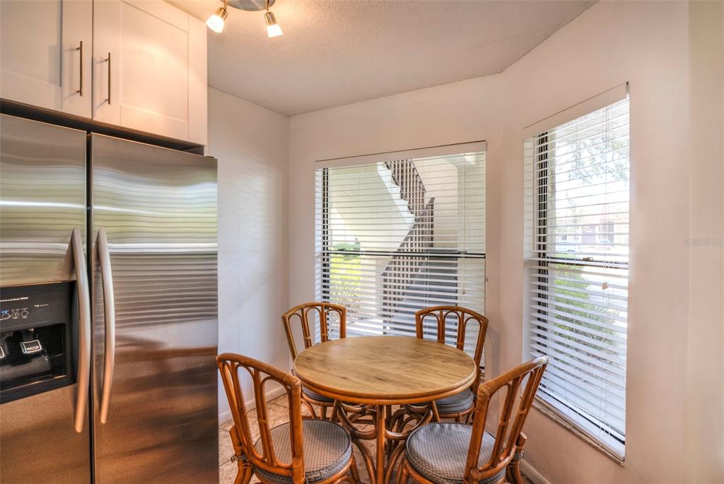 A kitchen breakfast nook features a round wooden table, rattan chairs, and a stainless refrigerator — 4601 46TH STREET COURT W UNIT 103B, BRADENTON, FL