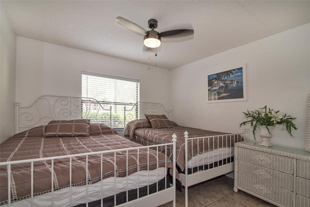 A bedroom features two white metal-framed beds, a wicker dresser, and a ceiling fan — 4601 46TH STREET COURT W UNIT 103B, BRADENTON, FL