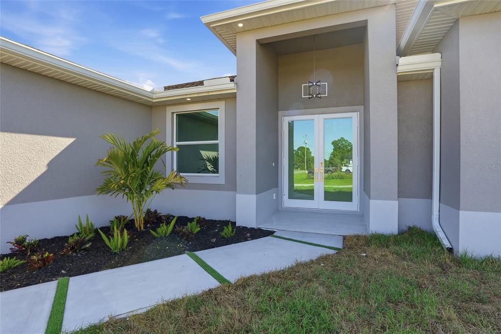 A modern home exterior features a double-door entrance, a concrete walkway, and a landscaped garden — 429 PALMYRA AVENUE, LEHIGH ACRES, FL
