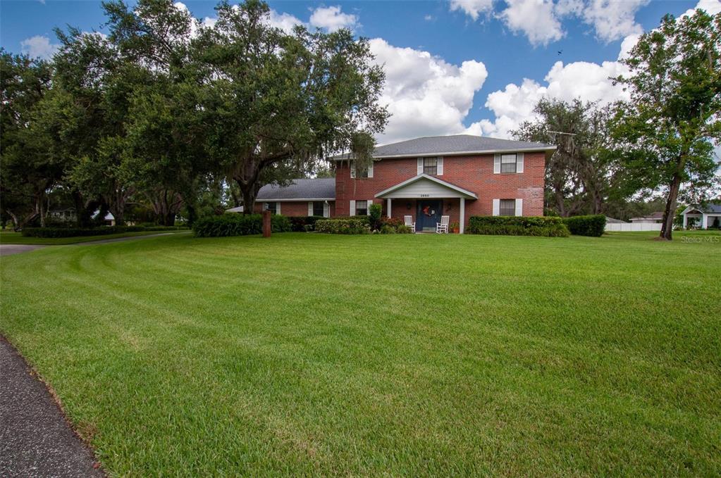 A two-story red brick house sits behind a large green lawn with mature trees — 3990 NE ASHLEY TERRACE, ARCADIA, FL