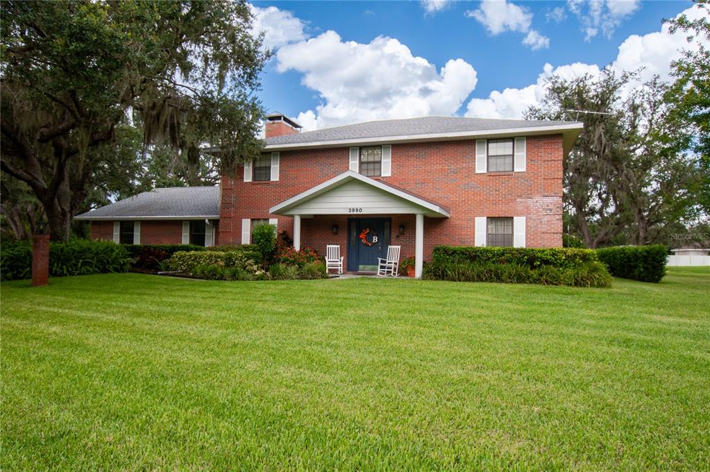 A two-story brick house with a covered front porch sits on a large grassy lawn — 3990 NE ASHLEY TERRACE, ARCADIA, FL