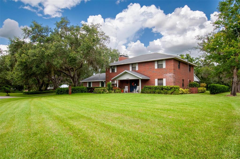 A two-story red brick house with a front porch sits on a large grassy lawn — 3990 NE ASHLEY TERRACE, ARCADIA, FL
