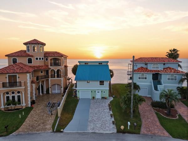An aerial view shows three waterfront houses with paved driveways at sunset — 6421 DRIFTWOOD DRIVE, HUDSON, FL