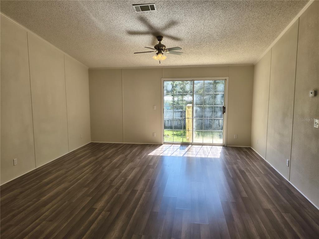 An empty living room features wood-look flooring, a ceiling fan, and sliding glass patio doors — 4703 S HATTERAY POINT, LECANTO, FL