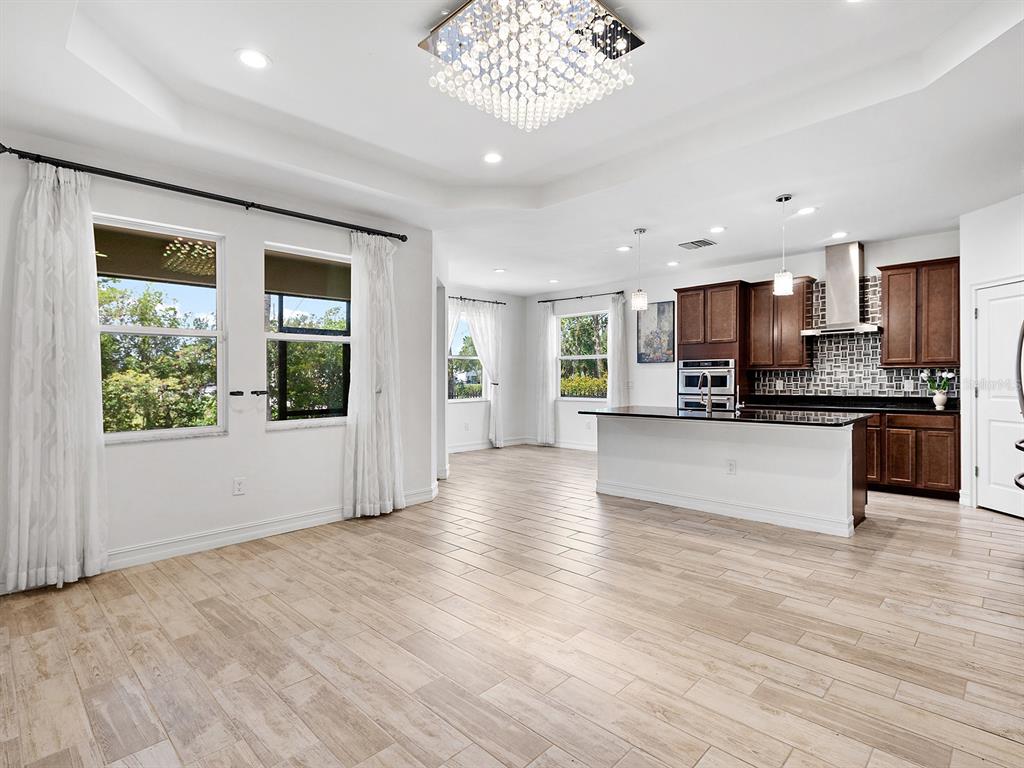 An open-concept kitchen and living area features wood-look tile flooring and a crystal chandelier — 4401 CONCHFISH LANE, OSPREY, FL