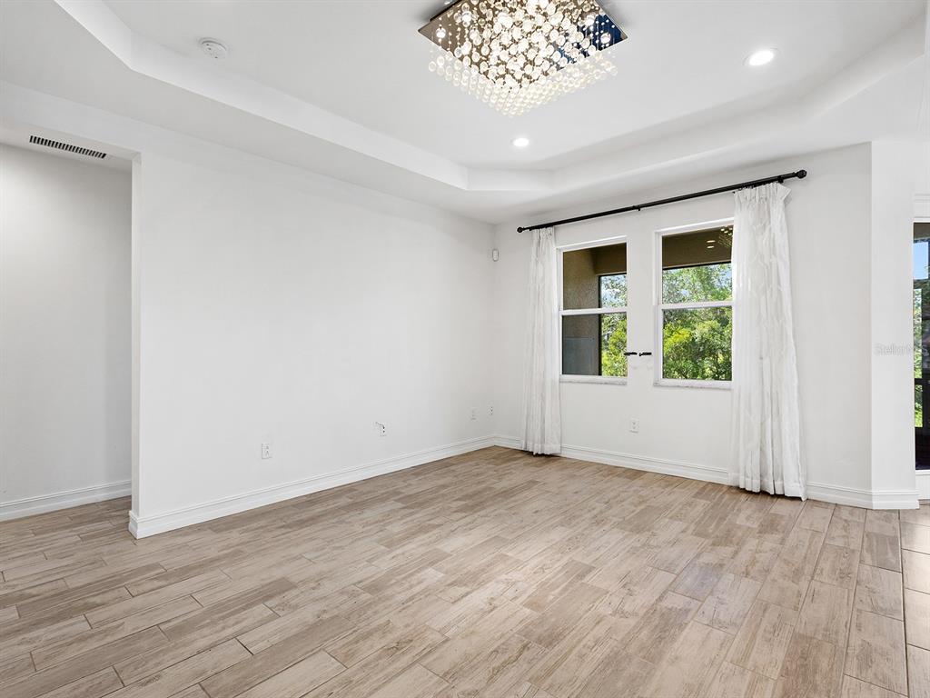 An empty room features white walls, wood-look tile flooring, a tray ceiling, and a crystal chandelier — 4401 CONCHFISH LANE, OSPREY, FL