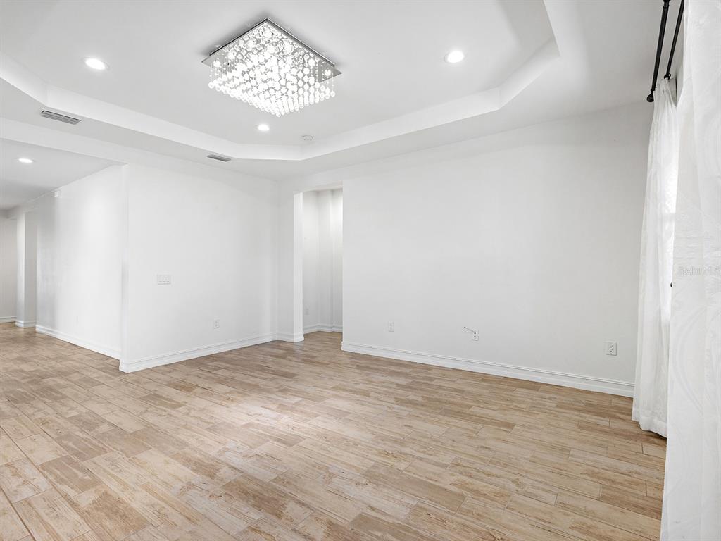 An empty room features a tray ceiling with a crystal chandelier and wood-look tile flooring — 4401 CONCHFISH LANE, OSPREY, FL