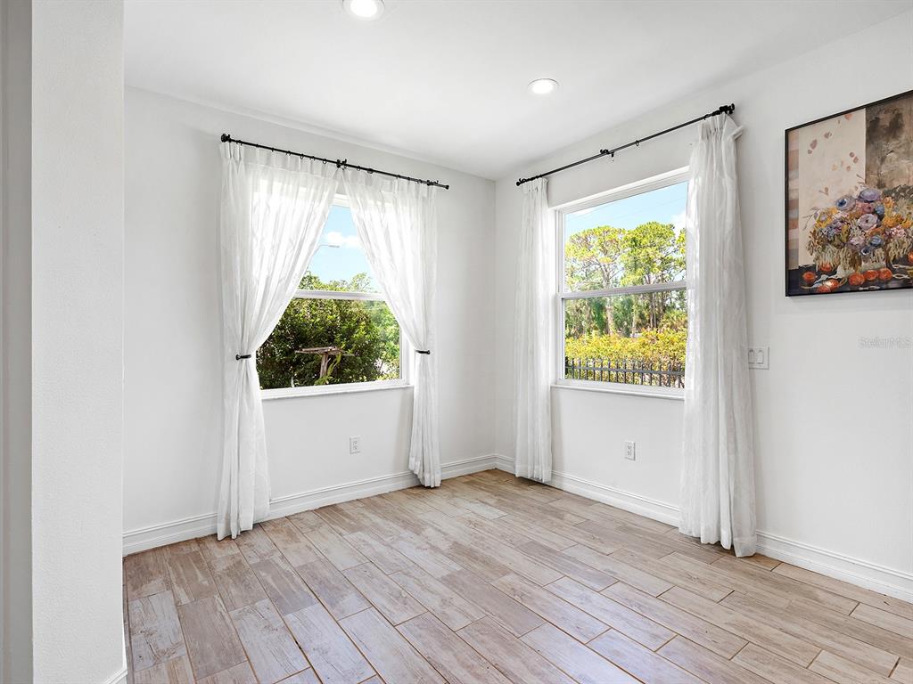 A bright room features white walls, wood-look tile flooring, and two windows with white curtains — 4401 CONCHFISH LANE, OSPREY, FL