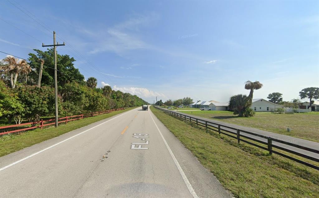 A two-lane road stretches into the distance, flanked by trees, fences, and residential houses — 13050 US HIGHWAY 441 SE, OKEECHOBEE, FL