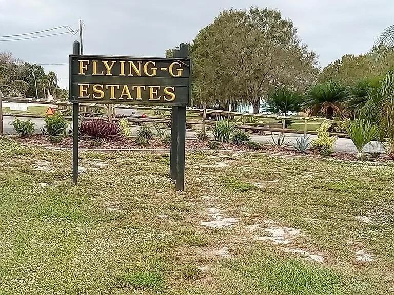A wooden sign for Flying-G Estates stands in a grassy area with trees behind it — 13050 US HIGHWAY 441 SE, OKEECHOBEE, FL
