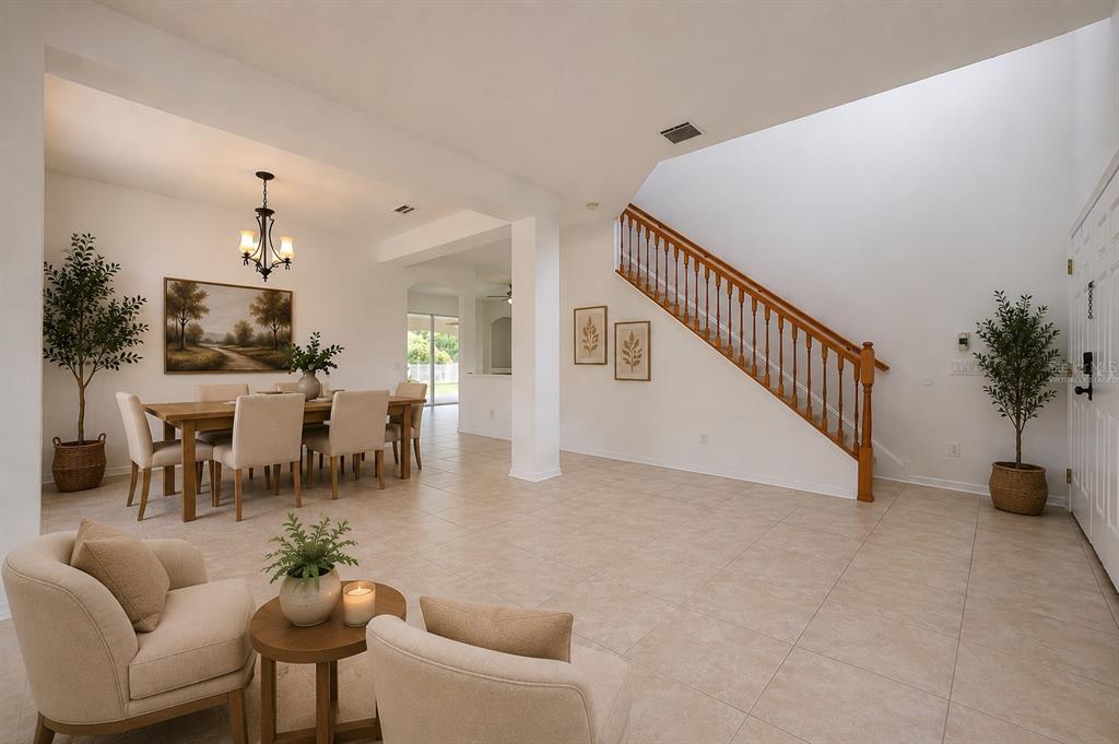 A bright, tiled foyer features a wooden staircase with a railing and a dining area — 4716 MAPLETREE LOOP, WESLEY CHAPEL, FL