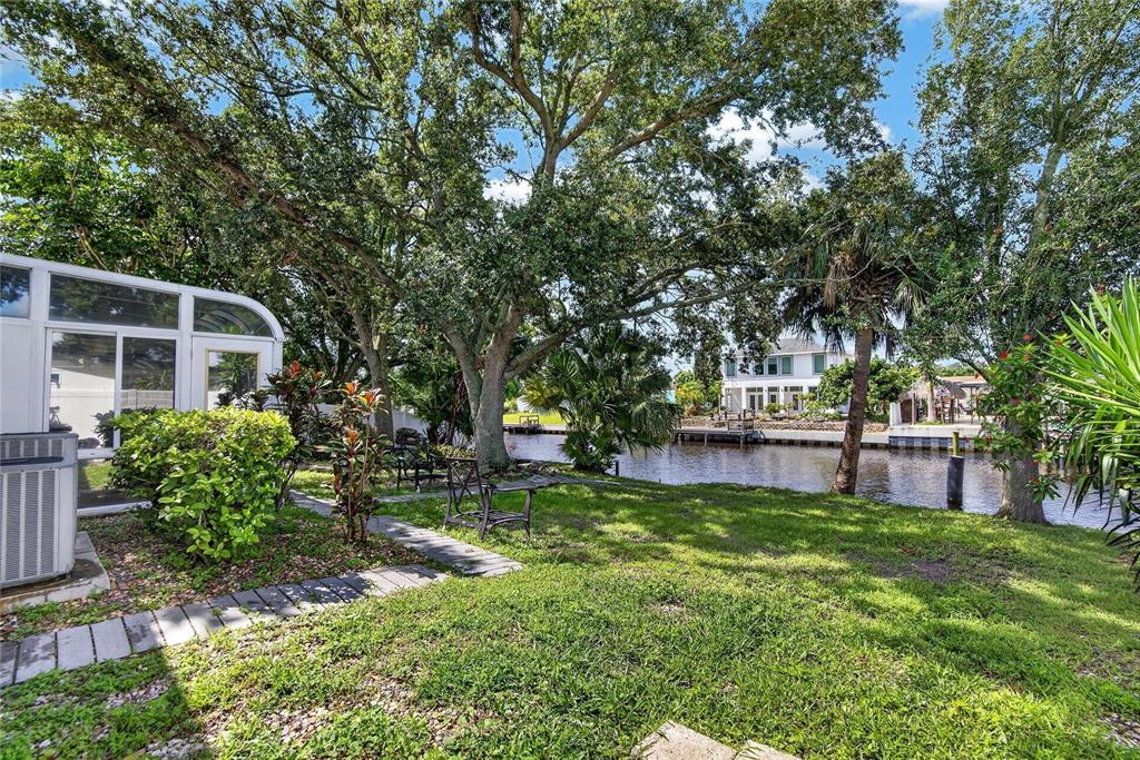 A grassy backyard features a patio, mature trees, and a view of a canal — 10718 DRUMMOND RD, TAMPA, FL