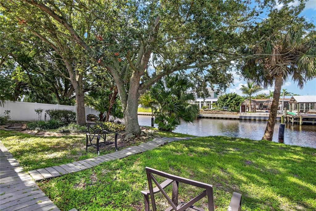 A grassy backyard features a wooden walkway, mature trees, and a view of a canal — 10718 DRUMMOND RD, TAMPA, FL