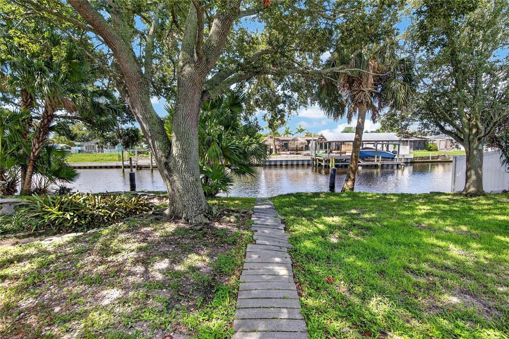 A stone path leads through a grassy yard toward a canal with a boat dock — 10718 DRUMMOND RD, TAMPA, FL
