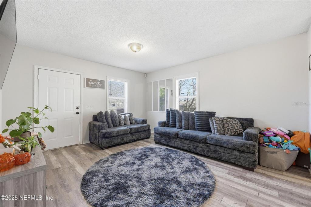 A living room features gray wood-look flooring, two dark sofas, and a round area rug — 1305 MELSON AVENUE, JACKSONVILLE, FL
