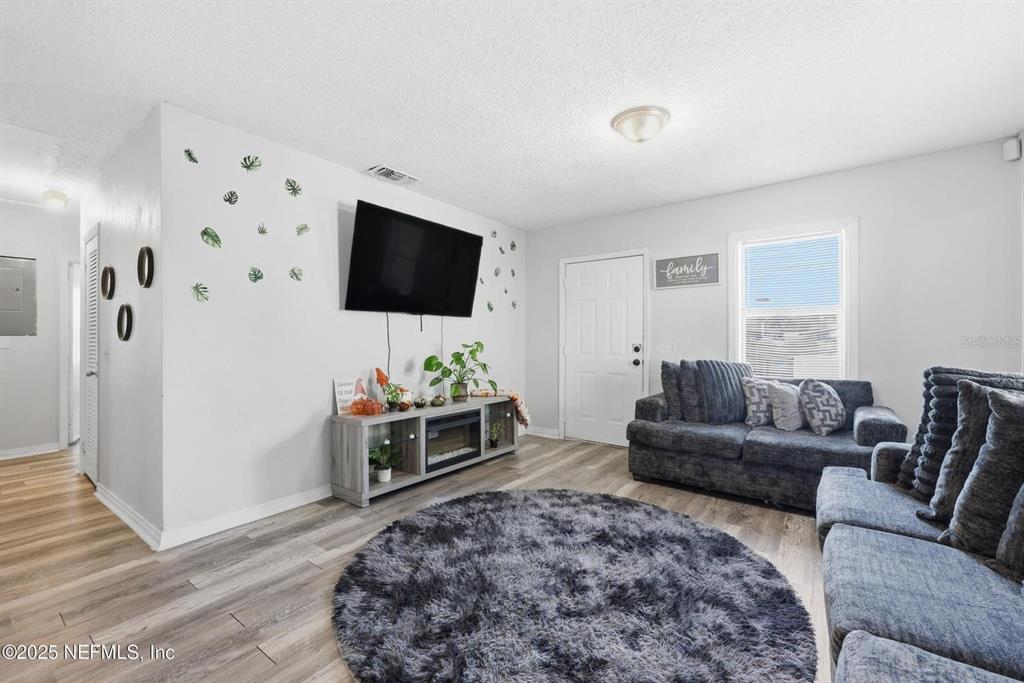 A living room features a gray sofa, a circular rug, and a wall-mounted television — 1305 MELSON AVENUE, JACKSONVILLE, FL