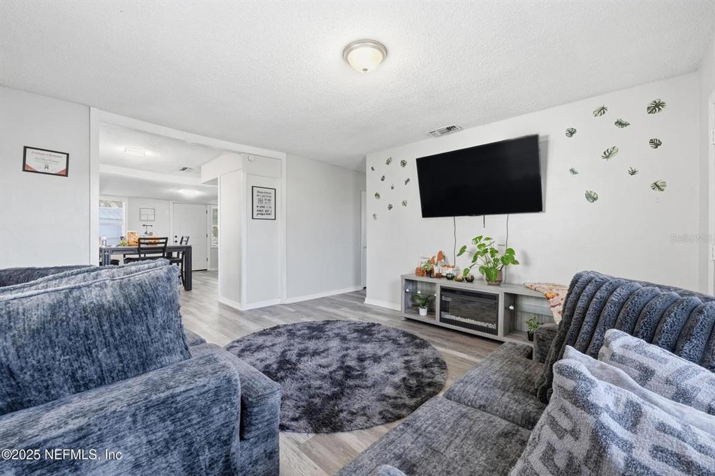 A living room features gray flooring, a circular rug, a wall-mounted television, and gray sofas — 1305 MELSON AVENUE, JACKSONVILLE, FL