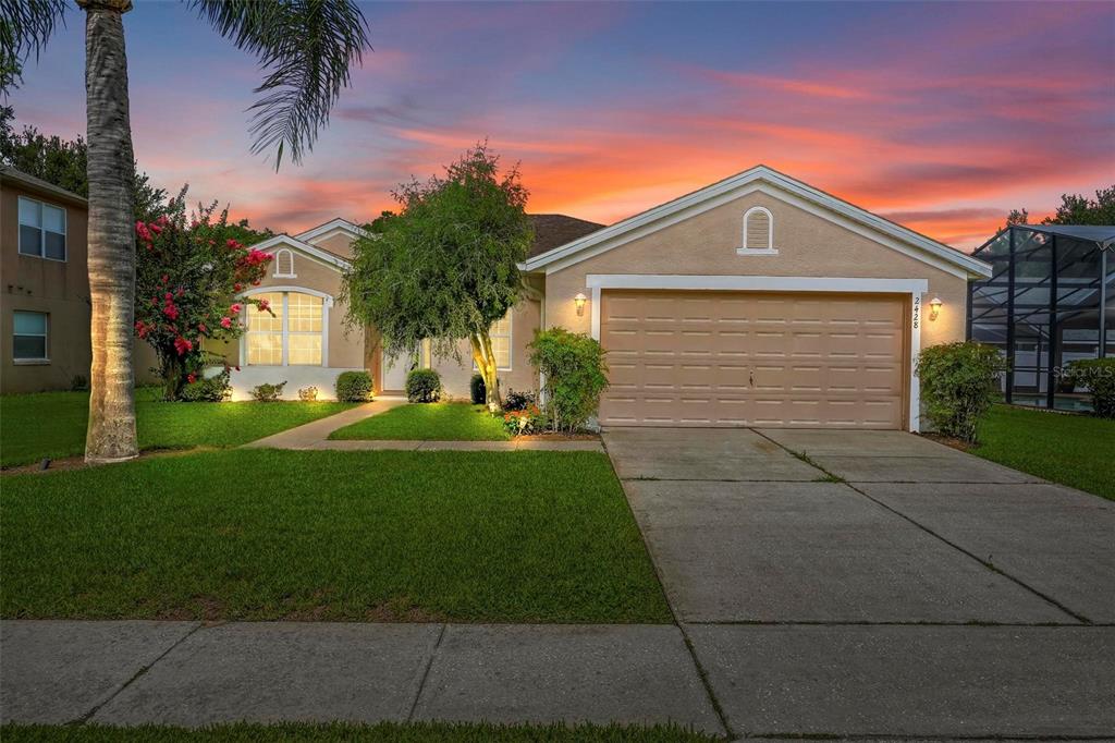 A single-story suburban house with a tan stucco exterior, a two-car garage, and a sunset sky — 2428 WALNUT HEIGHTS ROAD, APOPKA, FL