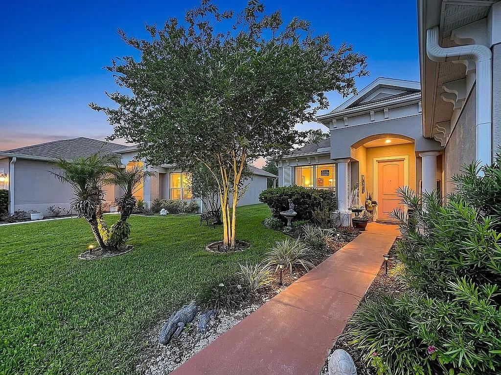 A single-story house exterior with a landscaped front yard, walkway, and illuminated entryway at dusk — 14530 BALLOCH DRIVE, HUDSON, FL