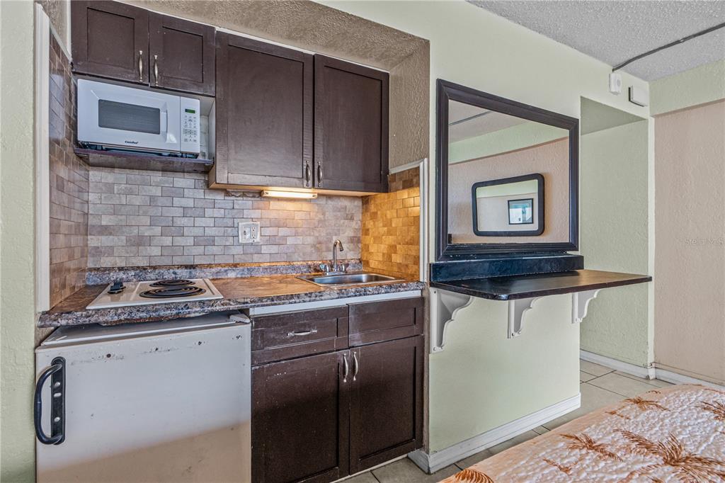 A small kitchenette features dark cabinets, a microwave, a stovetop, a sink, and a mirror — 2301 S ATLANTIC AVENUE UNIT 235, DAYTONA BEACH SHORES, FL