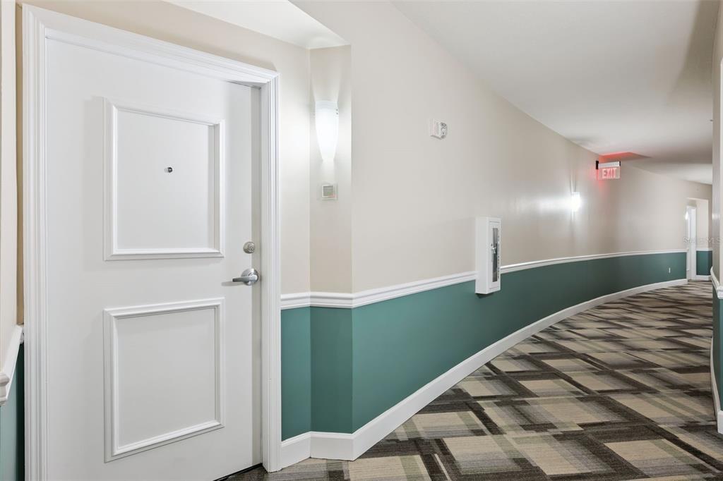 A hallway with a white door, teal wainscoting, and patterned carpet leads to an exit sign — 322 E CENTRAL BOULEVARD UNIT 1107, ORLANDO, FL