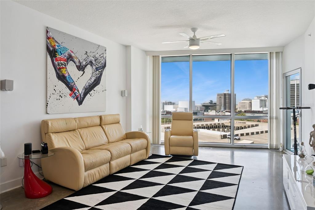 A living room features a tan leather sofa, a patterned rug, and floor-to-ceiling windows — 322 E CENTRAL BOULEVARD UNIT 1107, ORLANDO, FL