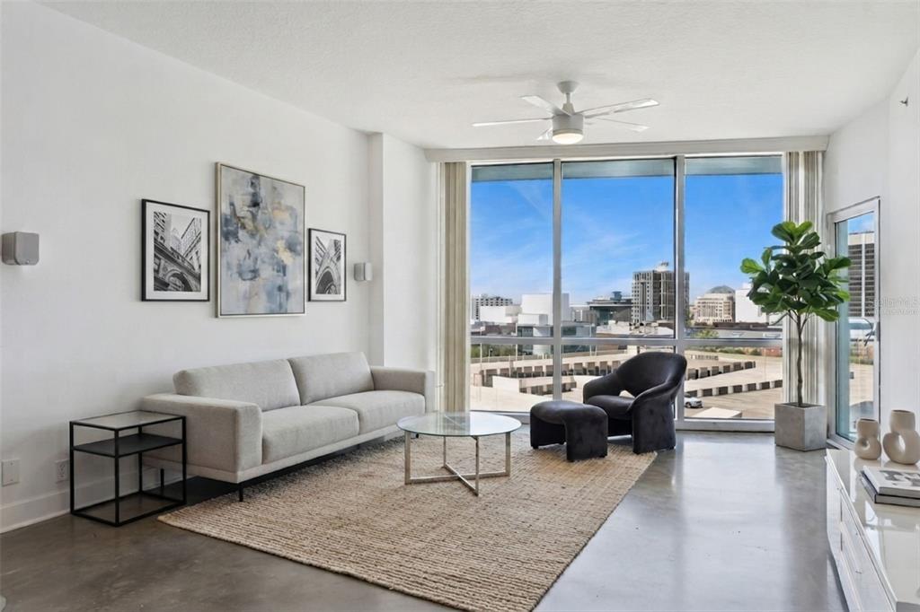 A modern living room features a leather sofa, patterned rug, and floor-to-ceiling windows with city views — 322 E CENTRAL BOULEVARD UNIT 1107, ORLANDO, FL
