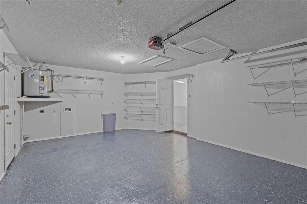 A garage with a gray speckled floor, white walls, shelving units, and a water heater — 5116 PLANTATION DRIVE, HOLIDAY, FL