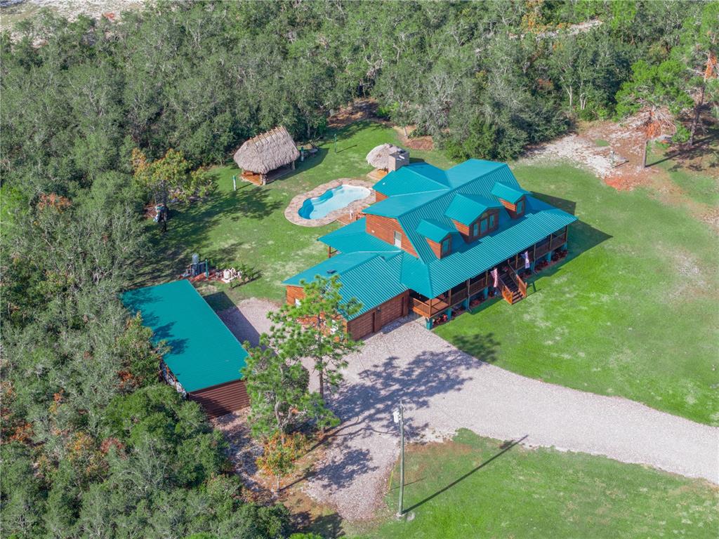 An aerial view of a log cabin with a green metal roof, pool, and detached garage — 1894 R E BYRD ROAD, FROSTPROOF, FL