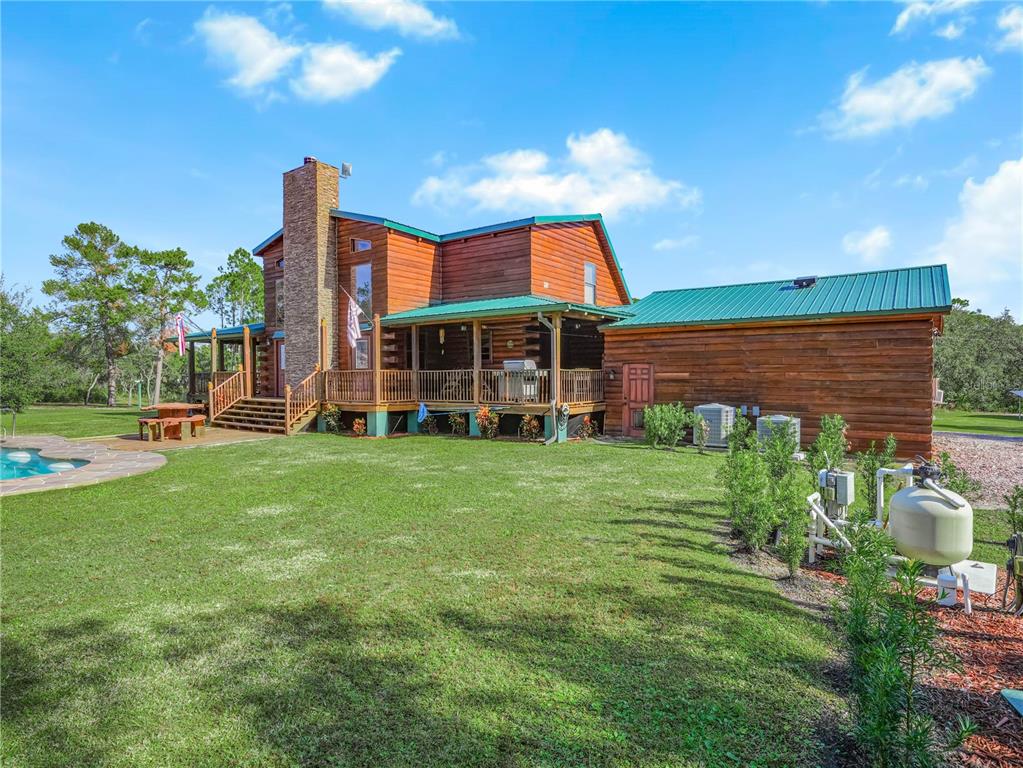 A two-story log cabin home features a green metal roof, stone chimney, and wraparound porch — 1894 R E BYRD ROAD, FROSTPROOF, FL