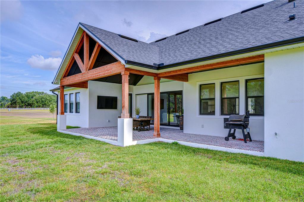 A covered brick patio with wooden beams and a grill attached to a white house — 111 ALAFIA ESTATES LANE, LITHIA, FL