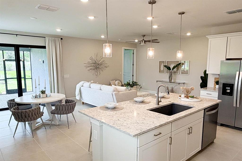 An open-concept living and dining area features a kitchen island, white cabinetry, and tile flooring — 5811 SILVERSIDE PINE COURT, LAKEWOOD RANCH, FL